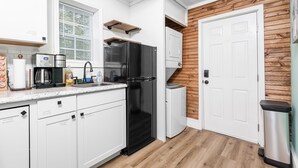 A compact kitchen with white cabinets, a black refrigerator, a built-in oven, and a wooden wall panel. - Serene & Quiet Cottage | Office | 5 Min to RH (Rock Hill)