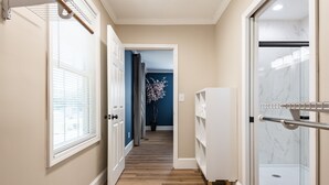 Un couloir doté d’un plancher en bois, de murs blancs et d’un mur d’accent bleu. On y trouve un meuble blanc et une cabine de douche en verre.