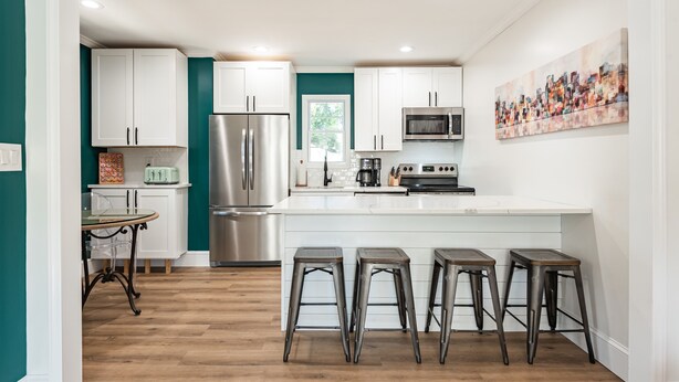 Una cucina moderna con mobili bianchi, elettrodomestici in acciaio inossidabile e un'isola centrale con sgabelli.