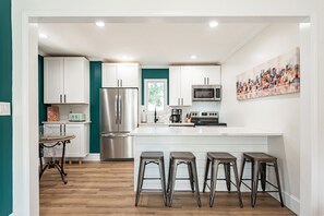 A modern kitchen with white cabinets, stainless steel appliances, and a central island with stools. - 3 Bd/2 Bth Historic Cape Cod | 5 Min Sports Center (Rock Hill)