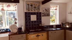 A kitchen with a black tiled backsplash, white cabinets, a stove, and a microwave. - 3 Bedroom Country Retreat - Dogs Welcome (Appleby-in-Westmorland)