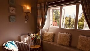 A cozy room with a striped armchair, a small table with a vase of flowers, and a window with a view of trees and a building. - 3 Bedroom Country Retreat - Dogs Welcome (Appleby-in-Westmorland)