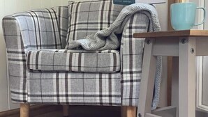 A plaid-patterned sofa with a matching throw blanket, a wooden side table with a blue mug, and a book on a shelf in a room with wooden flooring. - Shepherds Hut, self catering, Powys (Cascob)