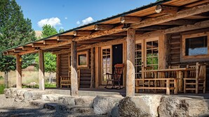 A rustic log cabin with a porch, a rocking chair, and a table.