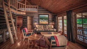 A cabin interior with a loft bedroom, a dining area, and a view of the outdoors.
