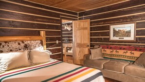 A room with a bed, a sofa, wooden walls, a door, and a framed picture on the wall.