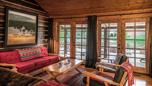A cozy room with a red sofa, wooden coffee table, and a view of a green landscape through large windows.