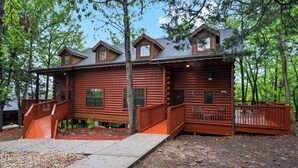 A log cabin with a wooden deck, a staircase, and a small porch.