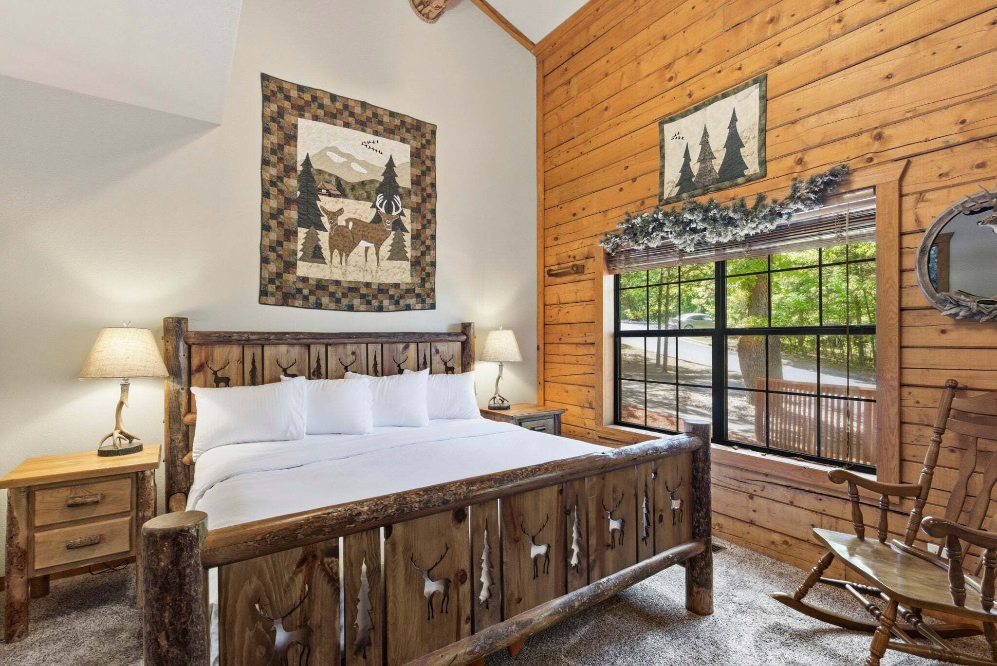 Un dormitorio estilo cabaña de madera con una cama, dos mesitas de noche, un sillón mecedor y una ventana con vistas.