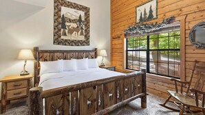 A wooden cabin-style bedroom with a bed, two nightstands, a rocking chair, and a window with a view.