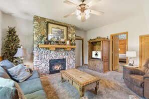A living room with a stone fireplace, a ceiling fan, and a cozy seating area.