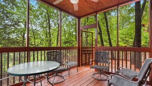 A covered outdoor deck with a table and chairs, surrounded by trees.