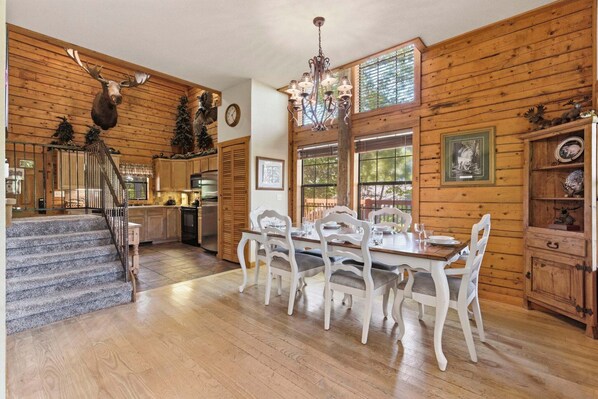 A wooden cabin interior with a dining table, chairs, a staircase, and a kitchen area.