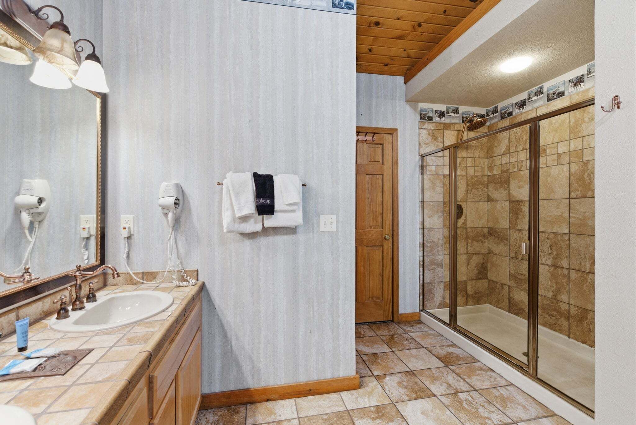 A bathroom with a sink, two hair dryers, a mirror, and a shower area.