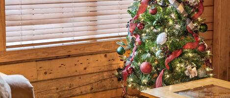 A cozy room with a wooden floor, a glass coffee table, and a Christmas tree decorated with ornaments and ribbons.