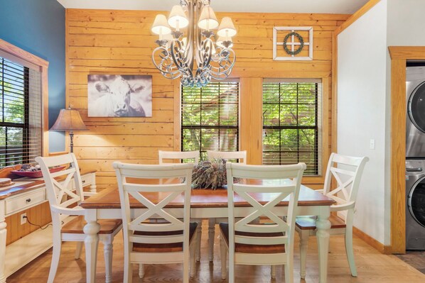 A dining area with a wooden wall, a chandelier, and a large window with blinds.
