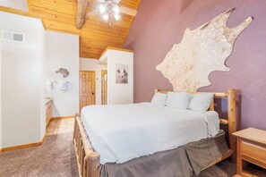 A bedroom with a wooden bed, a large wall-mounted animal hide, and a ceiling fan.