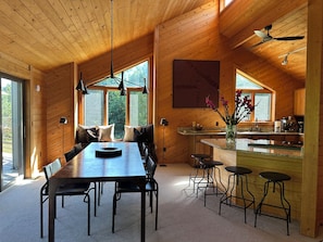 A wooden interior with a dining area, bar stools, and a kitchen.