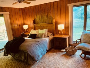 Une chambre confortable avec une tête de lit en bois, un lit agrémenté de plusieurs oreillers, deux tables de chevet avec des lampes, un panier en osier et un fauteuil.