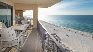 A balcony with Adirondack chairs, a table, and a view of a beach with people and a boat. - BEACH FRONT SAVINGS!...2 Bedroom…Phoenix I (Orange Beach)