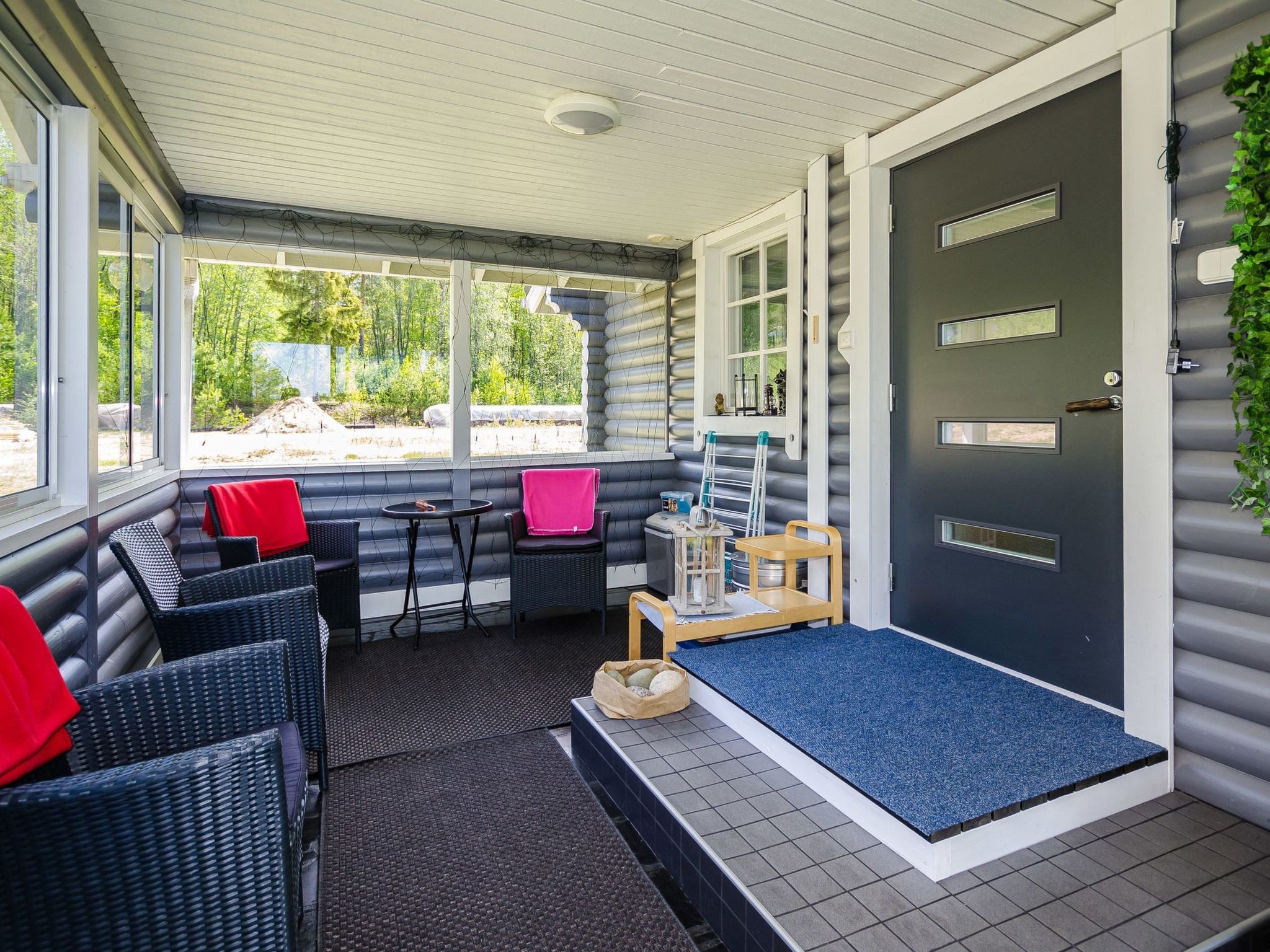 A covered outdoor seating area with wicker furniture, a small table, and a door with a mailbox.