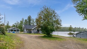 A cabin with a gravel driveway leading to a dock by a lake, surrounded by trees.
