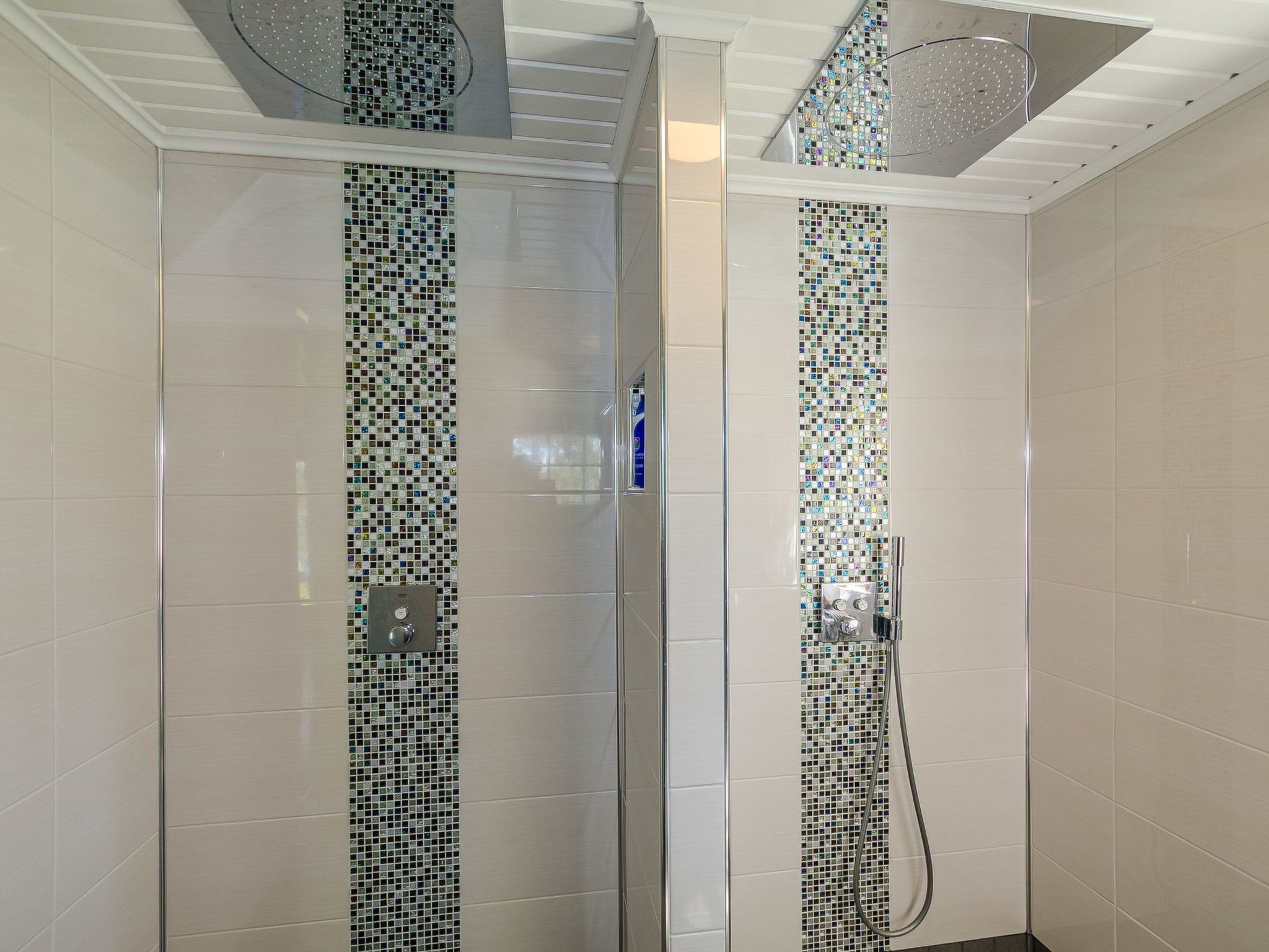 Ducha con puerta de vidrio y pared azulejada con diseño de mosaico.