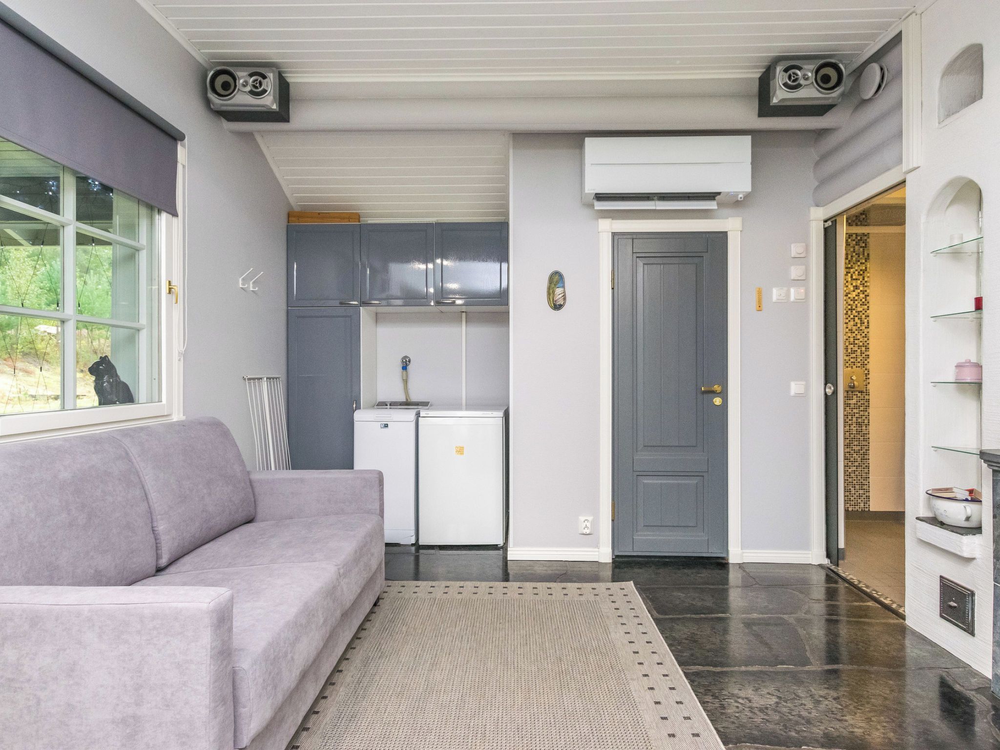 Un espace de vie compact comprenant un canapé, une kitchenette et une porte donnant accès à une salle de bain.