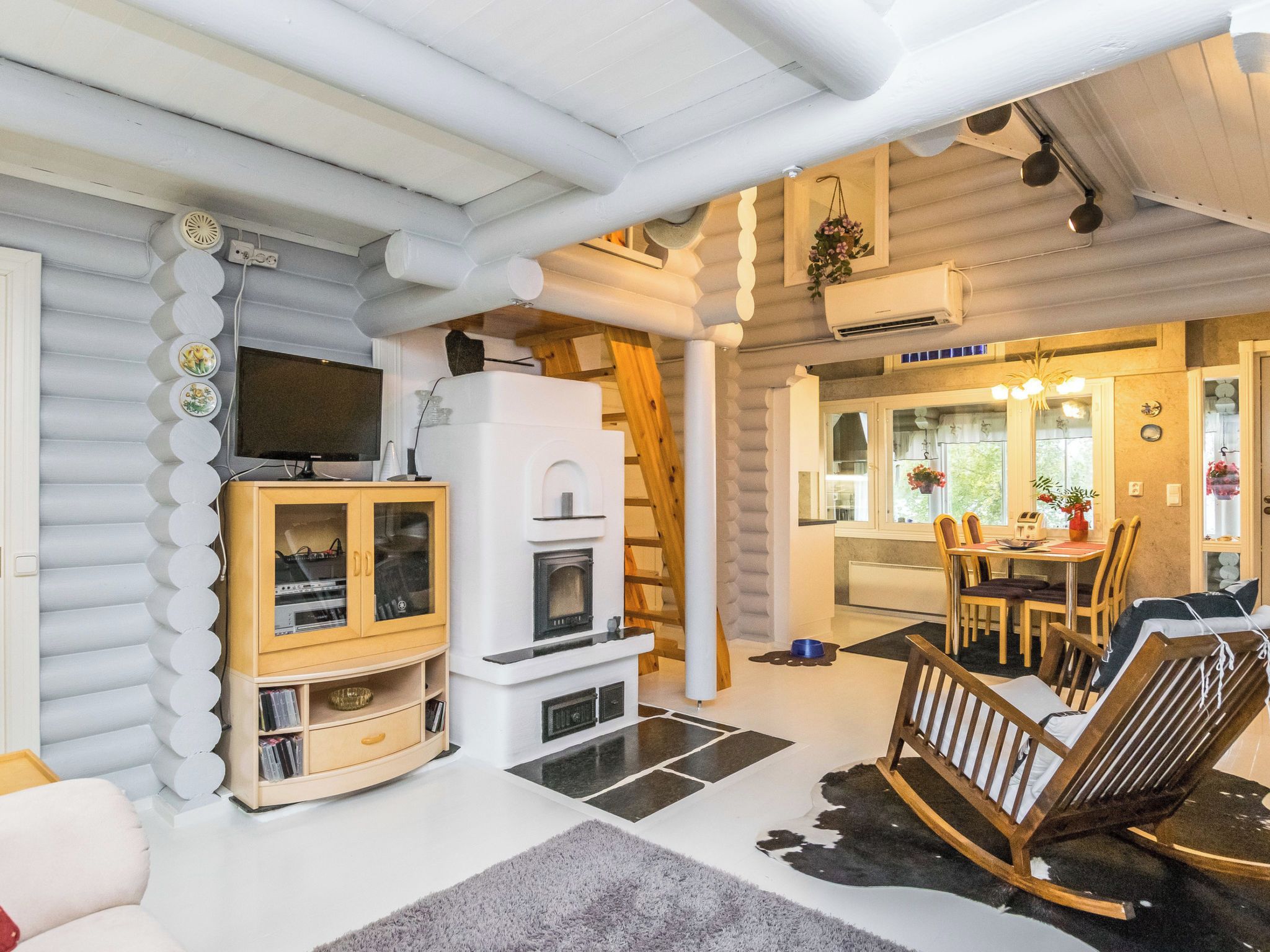 En stuga byggd av timmer med en öppen spis, ett matområde och en tv som är monterad på väggen.