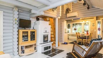 A log cabin interior with a fireplace, dining area, and a TV mounted on the wall.