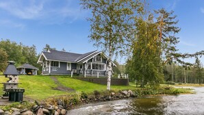 A lakeside cabin with a dock, surrounded by a stone retaining wall and a grassy area.