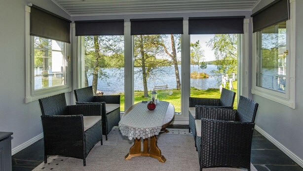 A covered outdoor seating area with wicker furniture and a table, overlooking a lake.