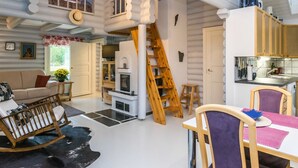 A cozy cabin interior with a living area, kitchen, and a loft bedroom with a wooden ladder.