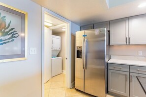 A compact kitchen with a stainless steel refrigerator, a built-in washing machine, and grey cabinets.