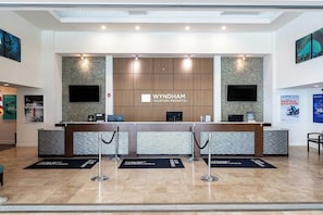 Una reception di Wyndham Vacation Resorts con un design moderno, che include un pannello decorativo in legno, un televisore a schermo piatto e un display digitale.