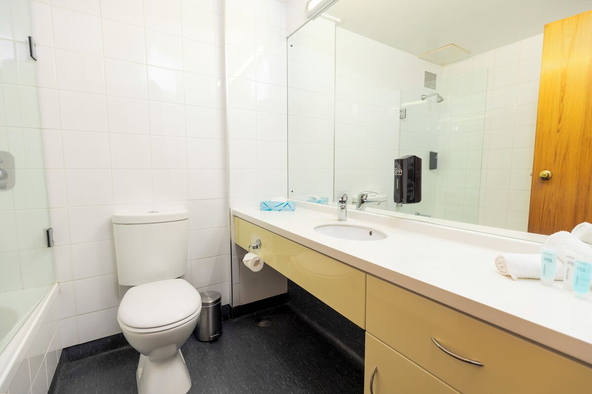 A bathroom with a toilet, sink, mirror, and a shower area.