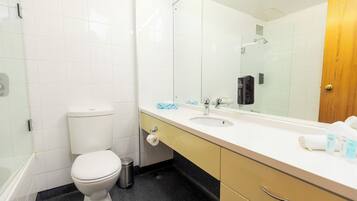 A bathroom with a toilet, sink, mirror, and a shower area.