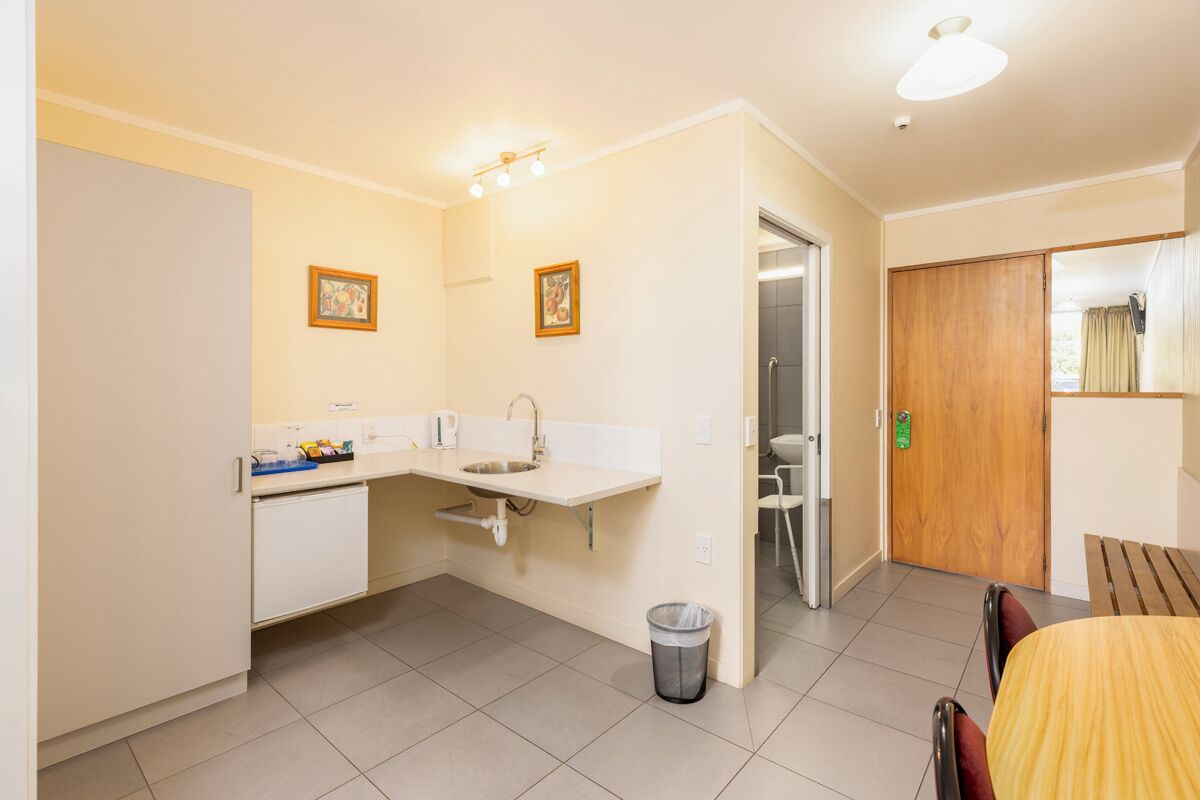 A compact kitchen with a sink, countertop, and a trash bin. There is a wooden door and a small table with chairs.