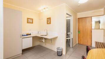A compact kitchen with a sink, countertop, and a trash bin. There is a wooden door and a small table with chairs.