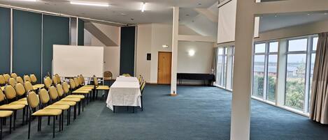 Un salón de conferencias con filas de sillas amarillas, una mesa blanca y una pantalla grande.