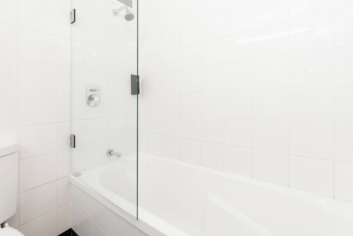 A modern bathroom with white tiles, a glass-enclosed shower, and a white bathtub.