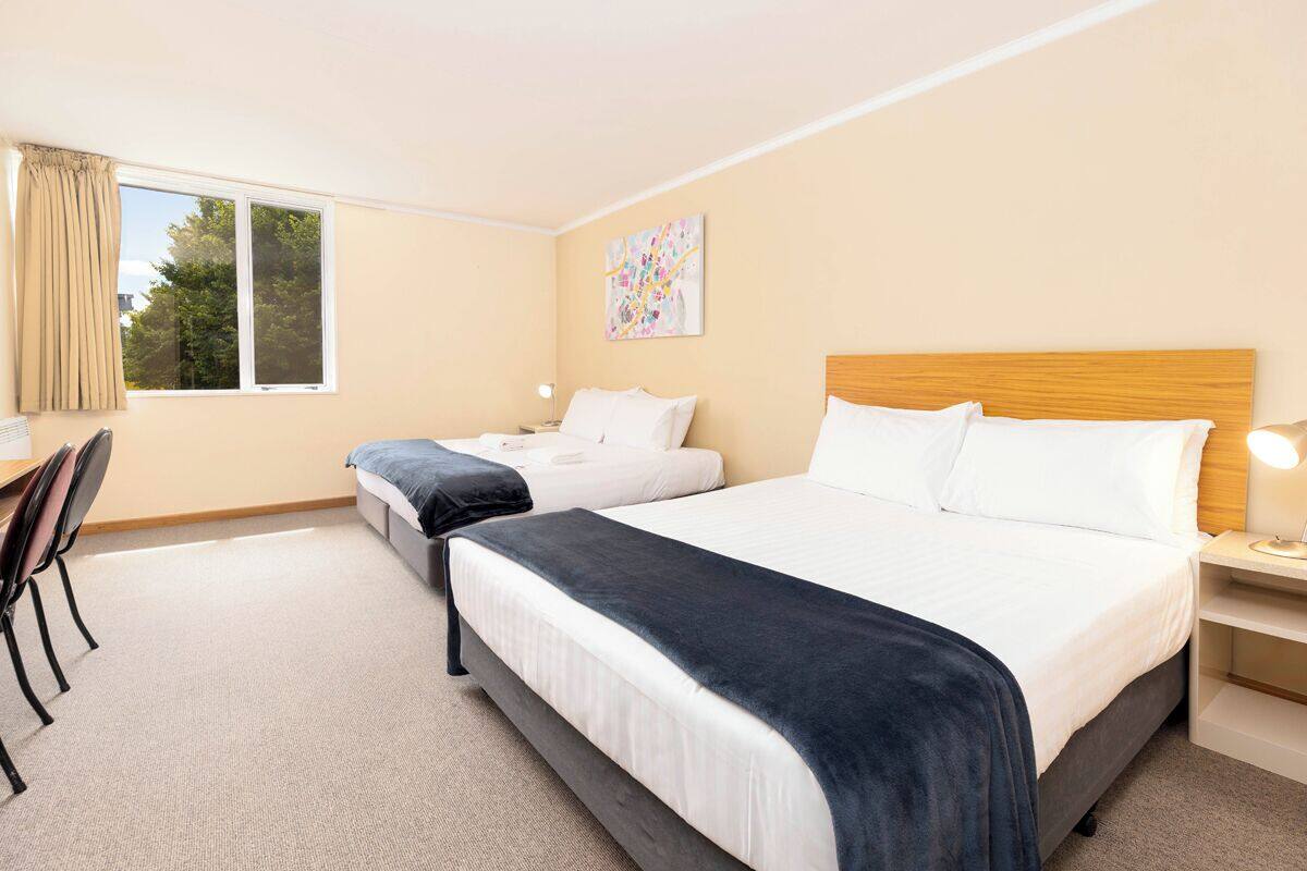 A hotel room with two beds, a desk, and a chair.