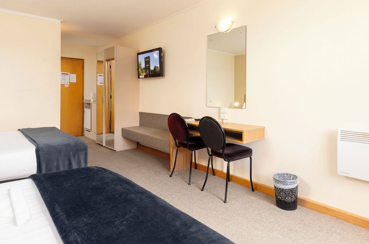 Une chambre d’hôtel avec deux lits, un bureau avec une chaise, un miroir et un téléviseur fixé au mur.