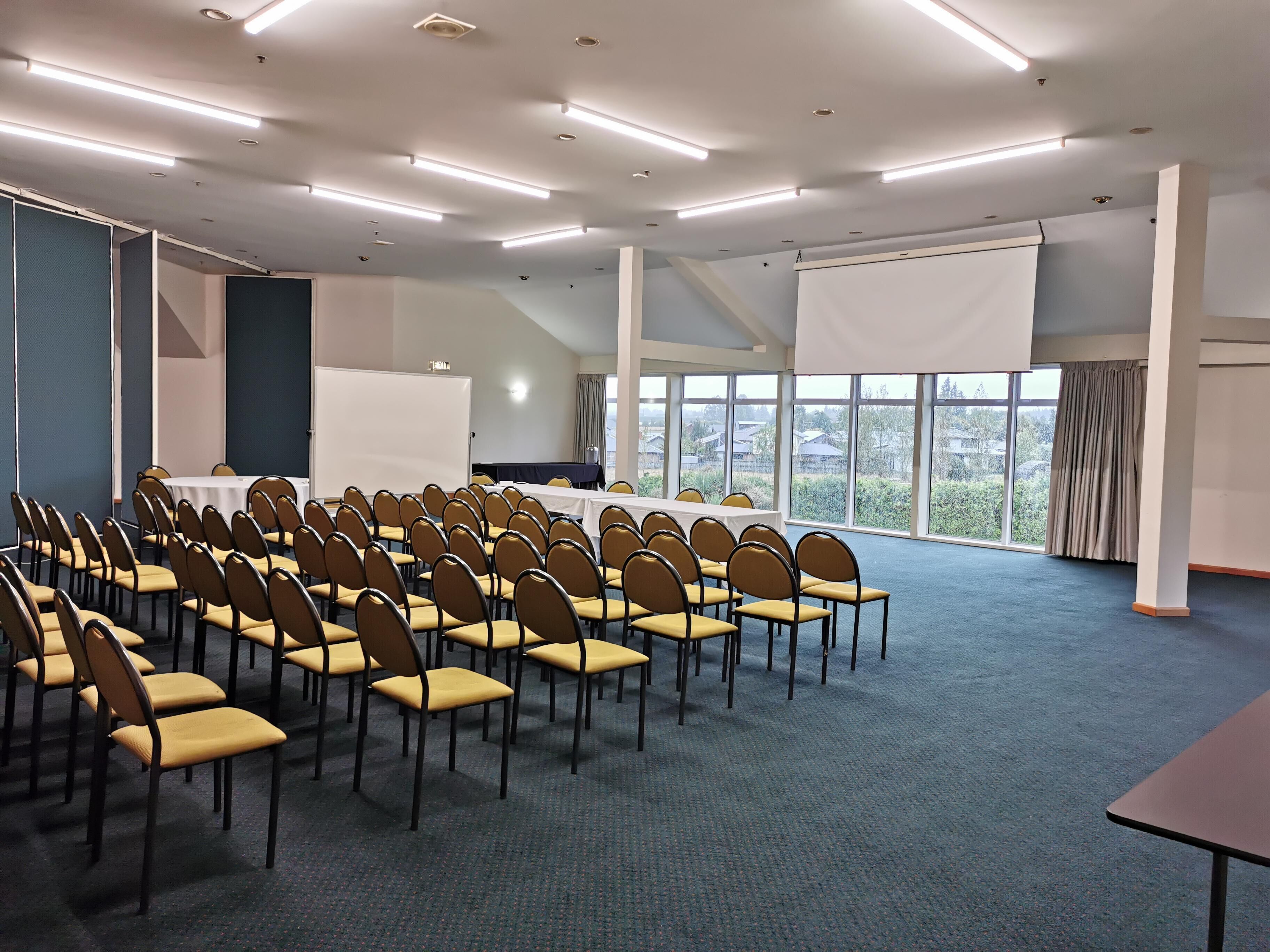 A conference room with rows of chairs, a whiteboard, and a large screen.