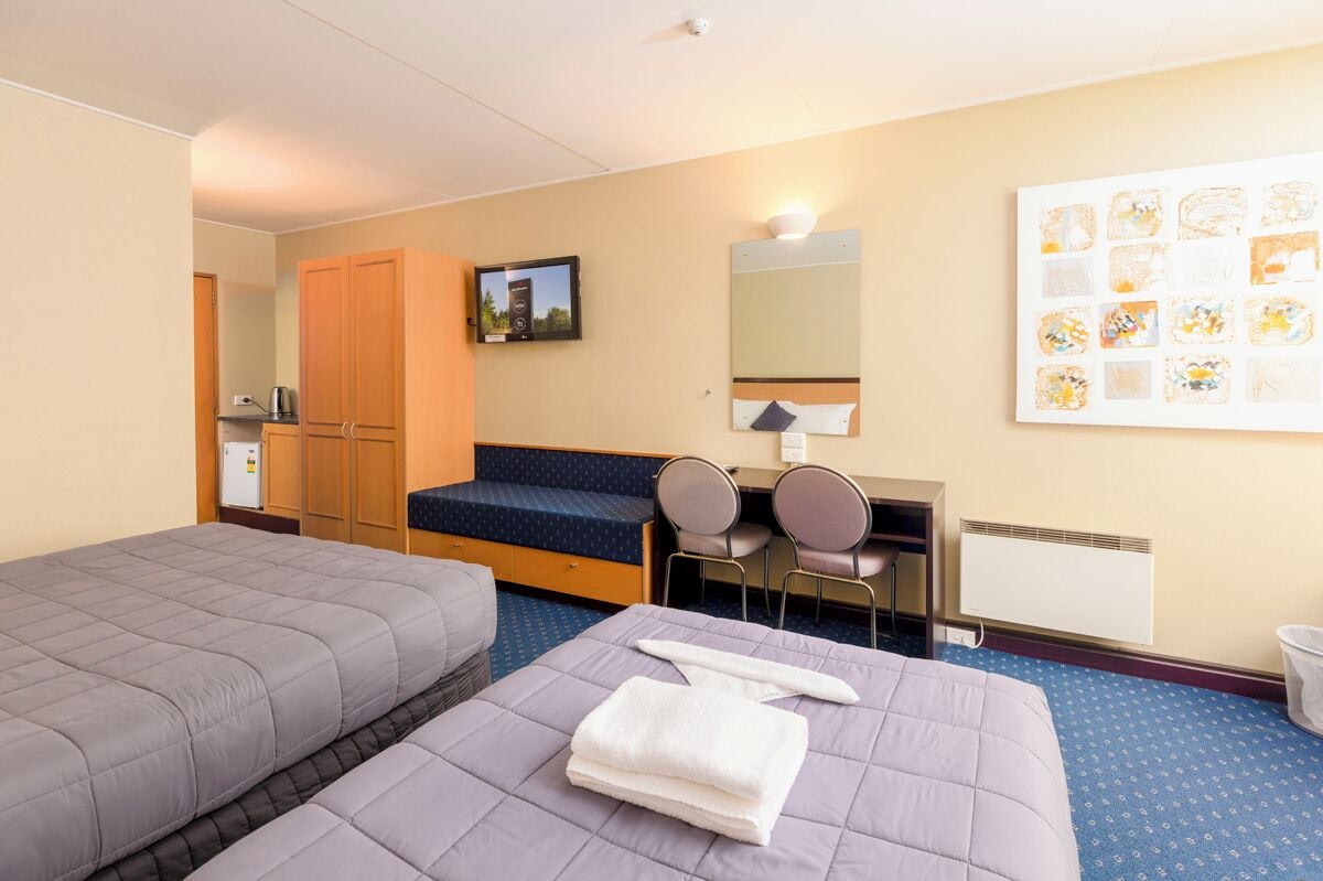 Una camera d'albergo con due letti, una scrivania con un computer, uno specchio e una TV.