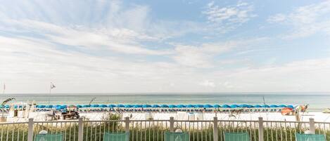 Een uitzicht op het strand met rijen blauwe parasols en ligstoelen.