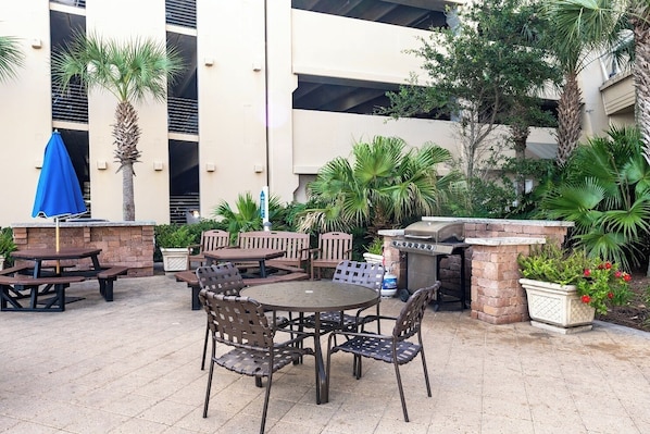 Un patio al aire libre con mesas y sillas, una parrilla y plantas en macetas.