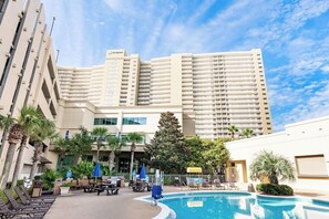 Et hotel med pool, udendørs siddepladser og palmer.