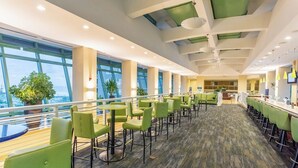 Ein großzügiger Innenbereich mit verschiedenen Sitzgelegenheiten, großen Fenstern und Blick ins Freie.