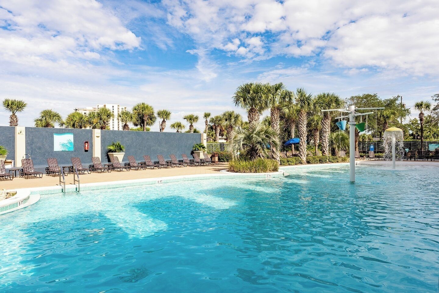 Ein Schwimmbecken mit Liegestühlen, Palmen und einer Springbrunnen.